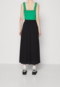 Vihreä rypytetty lyhyt toppi, jossa on röyhelösoljet, yhdistettynä pitkä musta hame. Jalkineissa on paksut mustat pohjat ja läpinäkyviä yksityiskohtia.