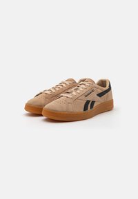 Sneaker in suede beige con accenti neri, lacci piatti, punta perforata e suola in gomma color caramello. Dettagli del logo sul lato e sulla linguetta.