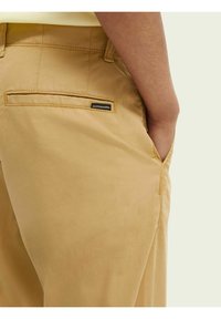 Beige Hose aus glattem Stoff. Verfügt über eine Gesäßtasche mit einem Etikett, sauberen Nähten und einem figurschmeichelnden Schnitt.