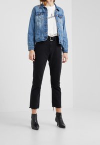 Modrá džínová bunda se dvěma předními kapsami, nošená přes bílou košili. Černé zkrácené džíny s roztrhanými lemy a černé kotníčkové boty.