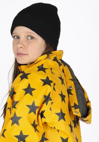 Gele waterdichte jas met zwart sterrenpatroon, drukknoop sluitingen en een grijze fleece voering. Draag met een zwarte geribde gebreide muts.