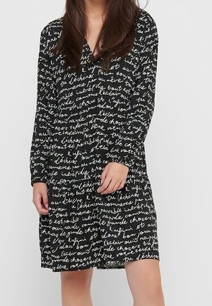 Vestido negro con texto manuscrito en blanco, mangas largas, escote en V y cintura fruncida. Tejido ligero con una textura suave.