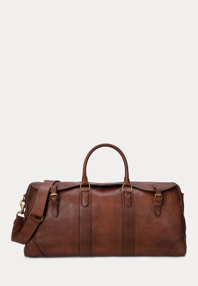 Sac de voyage en cuir marron avec deux poignées supérieures, une bandoulière réglable et des boucles en métal doré sur le devant et les côtés.