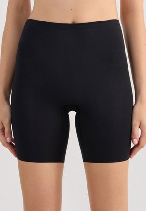 Waist to mid-thigh view van een persoon die effen zwarte, nauwsluitende shorts met een gladde tailleband draagt tegen een neutrale achtergrond.