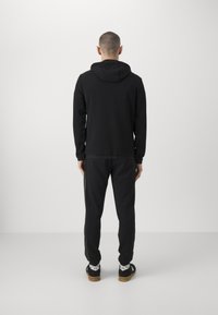Felpa con cappuccio nera e pantaloni jogger abbinati, caratterizzati da una texture morbida, un design semplice e un motivo discreto sul lato dei pantaloni.