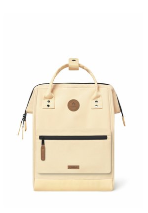 Beige canvas backpack with a top handle, black zipper accents, front zip pocket, circular logo, and textured bottom panel.