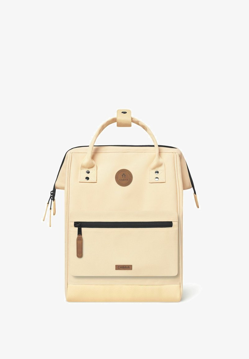 Beige canvas backpack with a top handle, black zipper accents, front zip pocket, circular logo, and textured bottom panel.