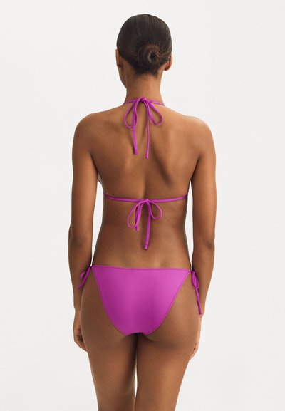 Purple bikini set featuring a halter neck and adjustable tie-side bottoms. Smooth texture and minimal stitching details enhance its design.