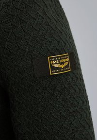 Groene gebreide trui met een gestructureerd ruitpatroon, met een zwart en geel label met de tekst "PME Legend" op de mouw.