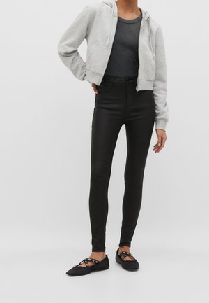 Grauer gekürzter Hoodie, schwarze hochtaillierte Jeans und schwarze flache Schuhe mit Ausschnittdetails. Glatte Textur und figurbetontes Design.