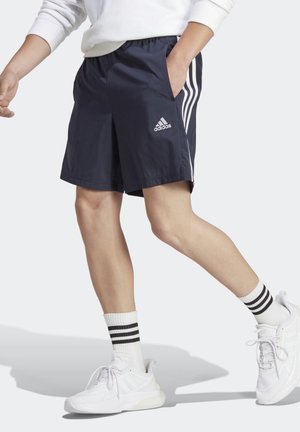 Person iført marineblå Adidas-shorts med hvide striber, hvide sokker med sorte striber og hvide sneakers, der går.