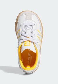 Weiße Leder Sneaker mit grauen Wildleder-Akzenten, gelben Streifen und weißen Schnürsenkeln. Verfügt über eine strukturierte Innensohle und eine Gummisohle.