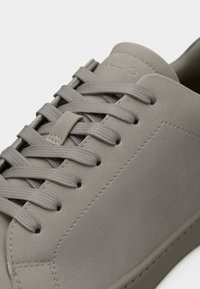 Gros plan sur une basket en daim gris avec des lacets texturés et des détails de couture subtils sur une surface supérieure lisse.