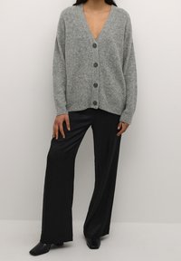 Cárdigan gris de punto con un escote en V profundo y seis botones oscuros, combinado con pantalones negros de pierna ancha con una textura suave.