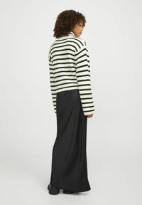 Pull en tricot noir et blanc à rayures avec un col montant, porté sur une longue jupe noire et des chaussures noires imposantes, vu de dos.