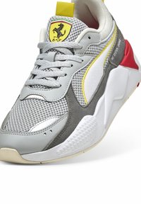 Szürke sportcipő hálós és velúr anyagból, sárga és piros díszítésekkel, kerek orral, párnázott bokarésszel és textúrált gumi talppal.