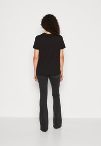 T-shirt en coton noir à manches courtes, encolure ras du cou et coupe décontractée, associé à un jean noir évasé. Simple, couleur unie, sans motifs visibles.