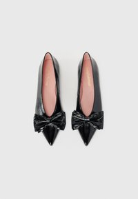 Chaussures en cuir verni noir avec des pointes pointues et un grand nœud noir sur chaque chaussure. Possède une semelle intérieure rose et un design épuré.