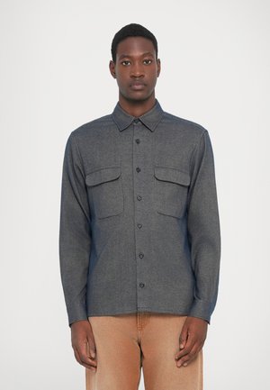 Donkergrijze blouse met lange mouwen, knoopsluiting, twee borstzakken, nette kraag en een gladde textuur. Gemaakt in combinatie met lichte broeken.