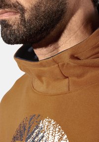 Brauner Hoodie mit hohem Kragen und strukturierter Stoffoberfläche, mit einem weißen Baumdesign in der Mitte und kontrastierendem Innenfutter.