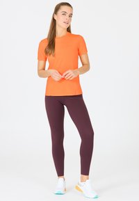 Ljusa orange kortärmade träningströja i kombination med djup bourgogne leggings och vita sneakers med turkosa och orange detaljer.
