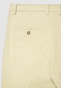 Beige Hose mit glatter Textur, ausgestattet mit einer Gesäßtasche und einem metallischen Knopfverschluss, gestaltet mit Gürtelschlaufen entlang des Bunds.