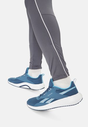 Persona che indossa scarpe da ginnastica Reebok blu con suole bianche e leggings atletici grigi con dettagli a strisce bianche.
