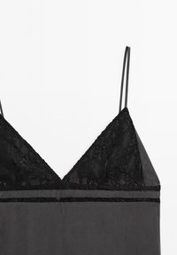 Black lace-trimmed camisole with thin straps, featuring a triangular neckline and a soft, smooth fabric body. Accented with a horizontal band.