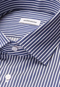 Camicia a righe verticali blu e bianche con bottoni bianchi e un'etichetta "seidensticker" cucita all'interno del colletto.