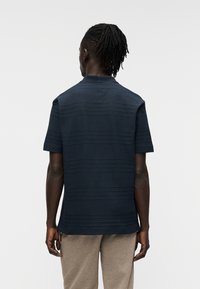 Μπλε ναυτικό κοντομάνικο πουκάμισο με υφασμένους οριζόντιους ρίγες, στρογγυλεμένο γιακά και άνετη εφαρμογή, σε συνδυασμό με ανοιχτό γκρι παντελόνια.