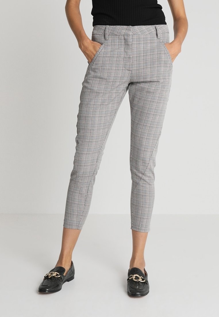Šedé kostkované kalhoty s dobře padnoucím střihem, zúženými nohavicemi, bočními kapsami a jemnou texturou. Doplněné černými mokasíny se zlatými detaily.