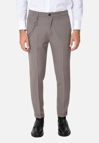 Pantaloni grigi con un tessuto liscio, vestibilità slim, orlo arrotolato e un accento a catena sulla tasca frontale. Abbinati a mocassini neri.