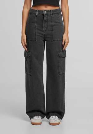 Sort denim jeans med høj talje og vide ben med store front- og sidelommer, båret med hvide sneakers og en kort sort top.