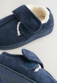 Pantofole blu navy con una superficie morbida e testurizzata, rivestite in pile e dotate di una chiusura in velcro. Forma arrotondata con accenti cuciti, progettate per il massimo comfort.