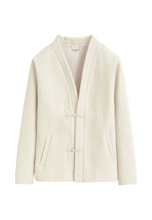 Veste matelassée couleur crème avec manches longues, deux poches à l'avant et deux petites fermetures à bascule en tissu sur le devant.