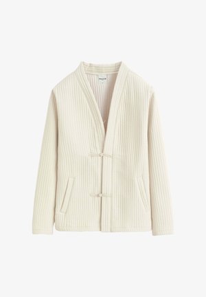 Veste matelassée couleur crème avec manches longues, deux poches à l'avant et deux petites fermetures à bascule en tissu sur le devant.
