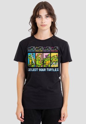 Young woman wearing a black T-shirt featuring pixel art of four Teenage Mutant Ninja Turtles with "Select Your Turtles" text below.