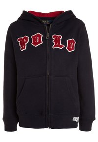 Veste à capuche zippée marine avec doublure en polaire rouge, arborant des lettres "Polo" brodées en blanc et rouge, poches latérales, poignets et ourlet côtelés.