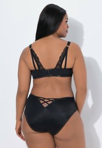 Rintaliivit mustalla pitsireunalla, joissa on säädettävät olkaimet ja hakasuljin, yhdistettynä korkeavyötäröisiin mustiin alushousuihin, joissa on ristikkäinen yksityiskohta takana.