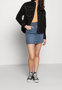 Chemise en denim noir avec des coutures blanches, haut orange, jupe en denim bleu avec taille élastique et baskets montantes noires.