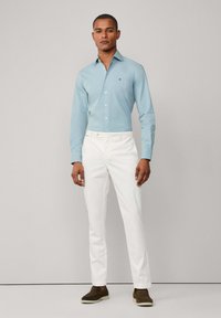 Lichtblauw lange mouw shirt, witte slim-fit broek, donkerbruine schoenen. Eenvoudig ontwerp, knoopsluiting, geen zichtbare patronen of accenten.
