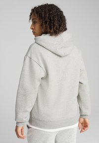 Sudadera con capucha de color gris claro, con una textura suave, corte holgado y puños acanalados. Cuenta con un bolsillo tipo canguro y una tela transpirable.