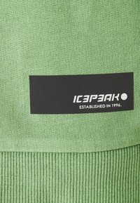 Tela verde con un tejido texturizado, que presenta una etiqueta negra que incluye la marca "ICEPEAK" y el texto "ESTABLECIDO EN 1996."