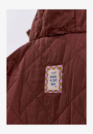 Brązowa kurtka pikowana z wielokolorową łatą w szachownicę oraz napisem "UWIERZ W SWÓJ BLASK".