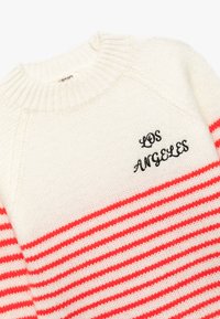 Sweter dziany w kolorze kremowym z różowymi paskami. Posiada okrągły, ściągaczowy dekolt oraz wyszywane "LOS ANGELES" na czarno. Miękka struktura.