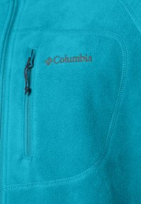 Türkiissinine fliisjakki, millel on lukuga rinnatasku, kontrastsed õmblused ja pruun brodeeritud Columbia logo vasakul ülemisel küljel.