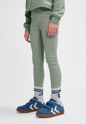Zielone prążkowane legginsy w połączeniu z niebiesko-białymi trampkami. Skarpetki są szare w niebieskie paski, charakteryzujące się swobodnym i sportowym stylem.