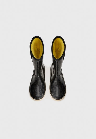 Une paire de bottes de pluie noires brillantes avec des éclaboussures blanches et une doublure jaune vif, vues de haut sur un fond blanc.