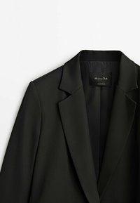 Black blazer with a classic collar, made of smooth fabric, featuring a simple design and a subtle inner label. No buttons or embellishments.