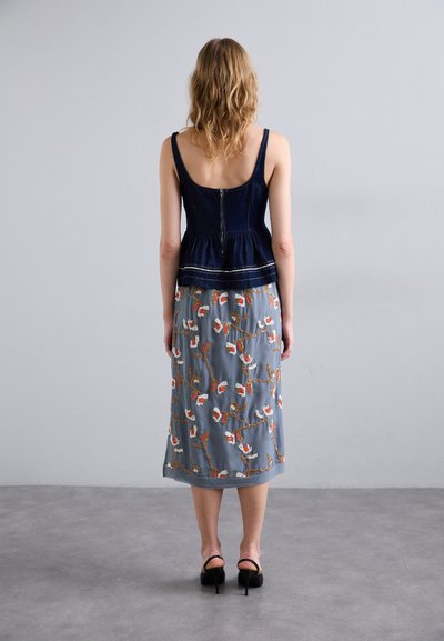 Dunkelblaues Jeans-Peplum-Top mit tailliertem Oberteil. Grauer Maxikleid mit floralen Stickereien in Orange und Weiß, mit transparenter Textur.